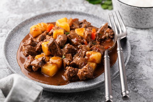 Savory and tender carne guisada served in a white ceramic plate, garnished with fresh cilantro and accompanied by a side of rice.