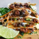 A delicious steak quesadilla cut into wedges, served on a white plate with a side of guacamole and salsa